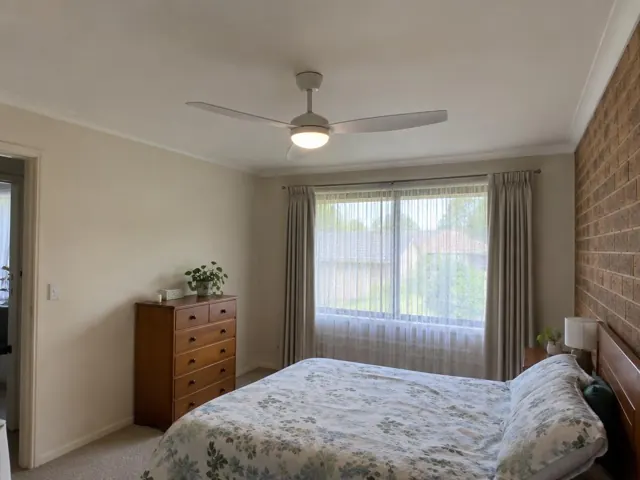 Ceiling fan fitted in a carpeted bedroom with brick feature wall and window curtains in Winston Hills
